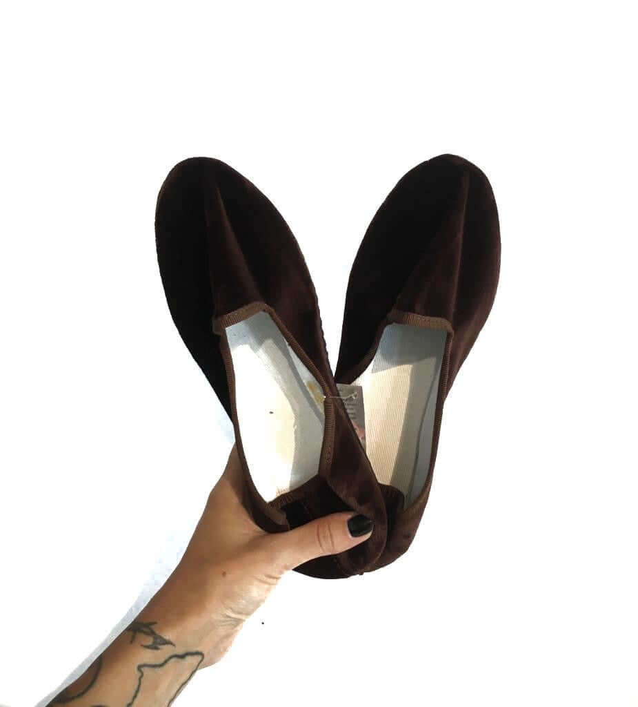 Person holding pair of brown velvet loafers against a white background.