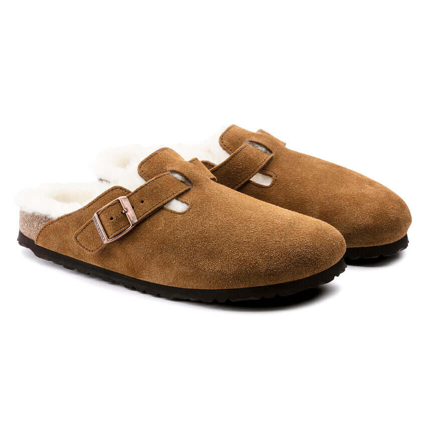 Brown suede fur-lined slip-on slippers with adjustable buckle straps on a white background.