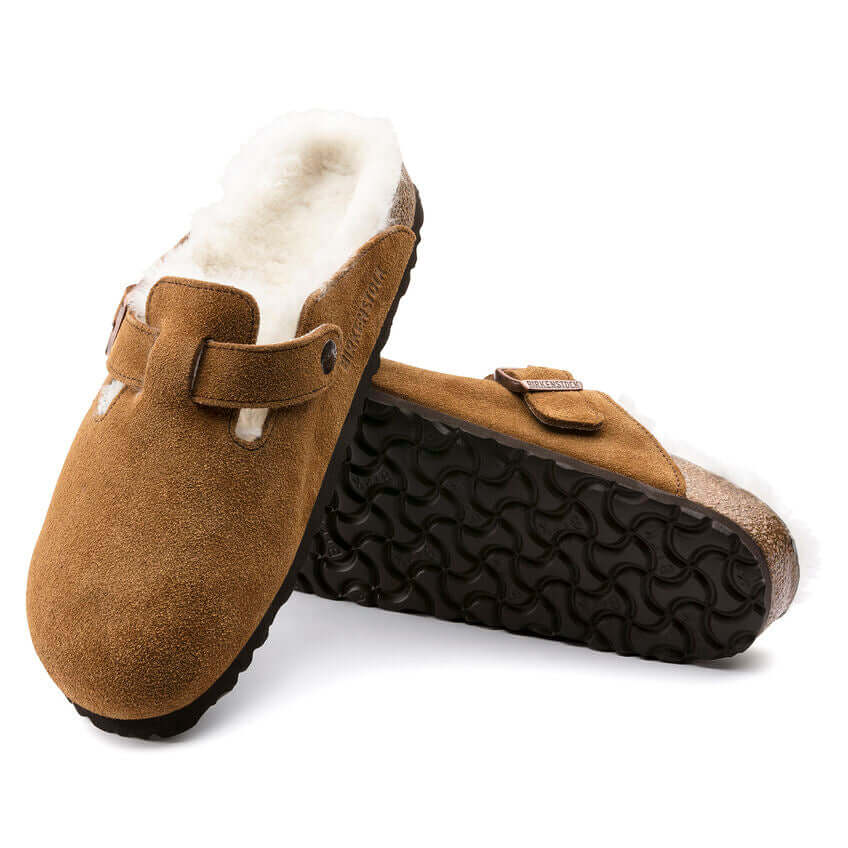 Brown suede clogs with white fluffy lining and black patterned soles.