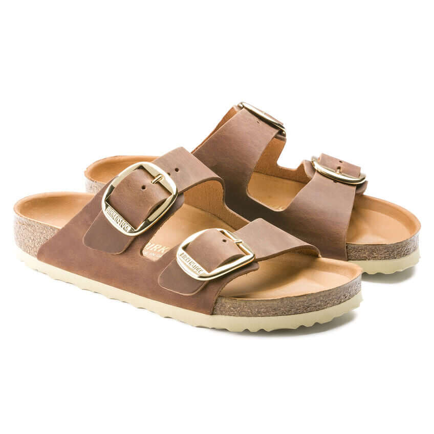 Brown leather sandals with adjustable straps and cork soles featuring gold buckles.