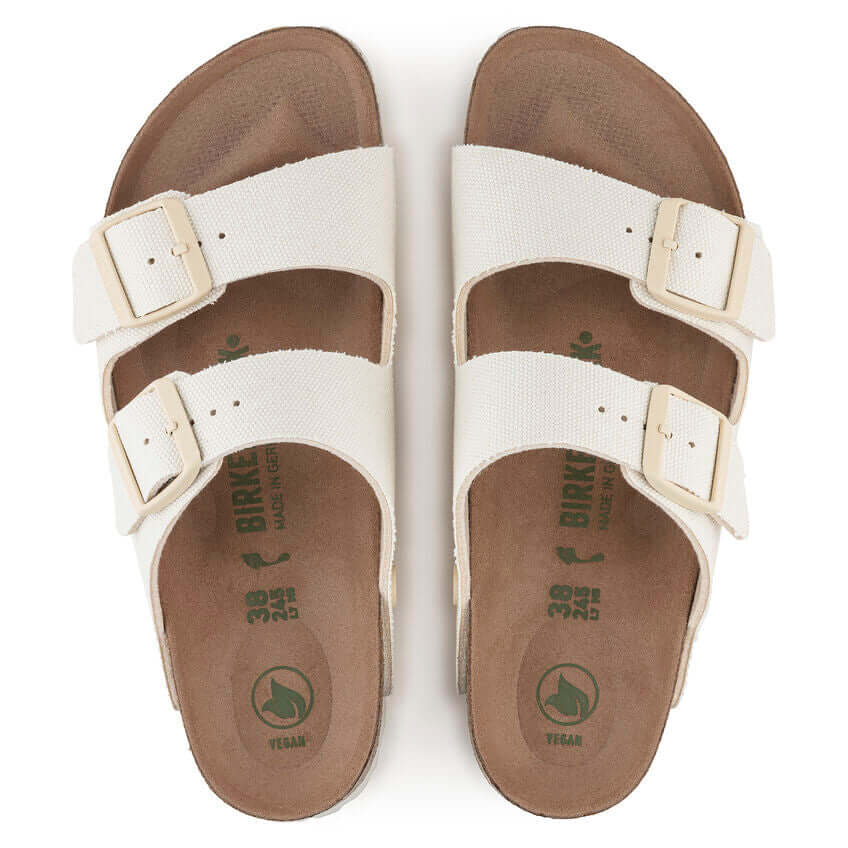 Top view of white vegan Birkenstock sandals with two straps and buckles on brown footbeds.